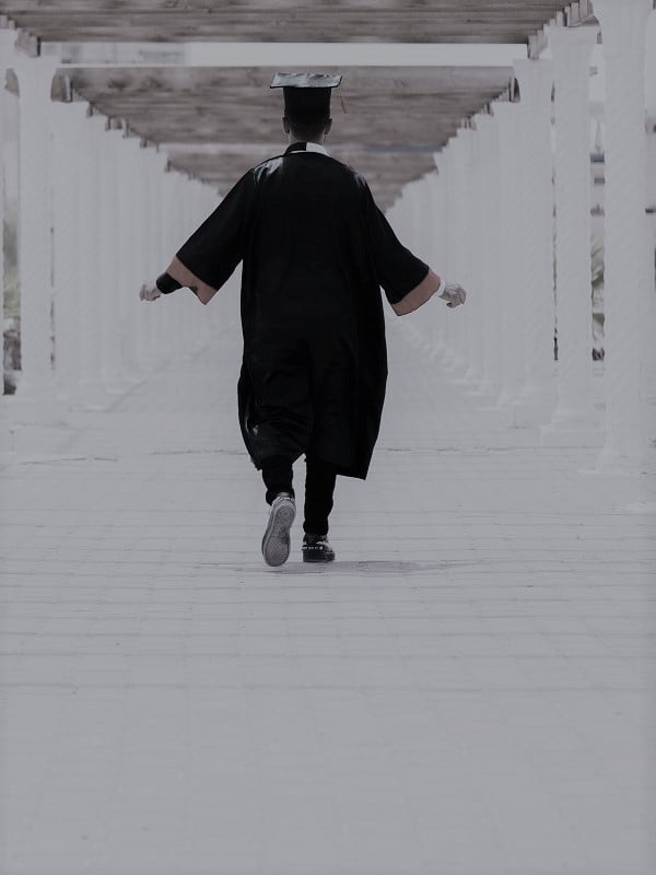 male graduate in cap and gown walking down hallway